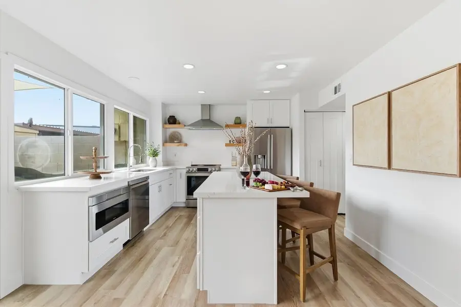 Kitchen at Hideaway seen from the window end, with the island and bar stools, range hood, refrigerator and art on the wall
