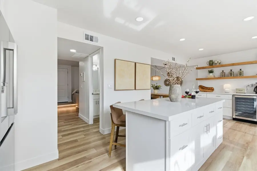 Kitchen island with bar stools, the coffee bar and wine fridge, and the hallway to the half bath at Hideaway