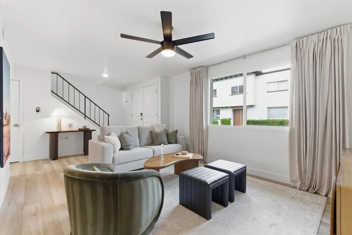 Living room at Hideaway with sofa, armchair, staircase and the front entry, windows facing the community lawn