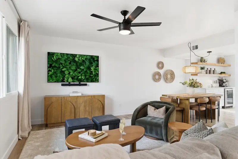 Living room at Hideaway with the smart TV above a wood sideboard, a velvet armchair, leather ottomans and the dining table beyond