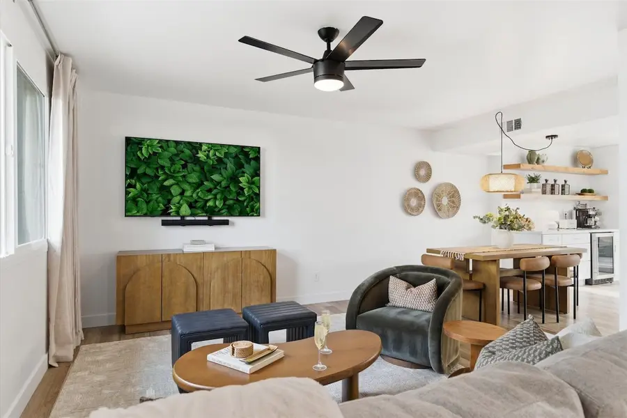 Living room at Hideaway with the smart TV above a wood sideboard, a velvet armchair, leather ottomans and the dining table beyond