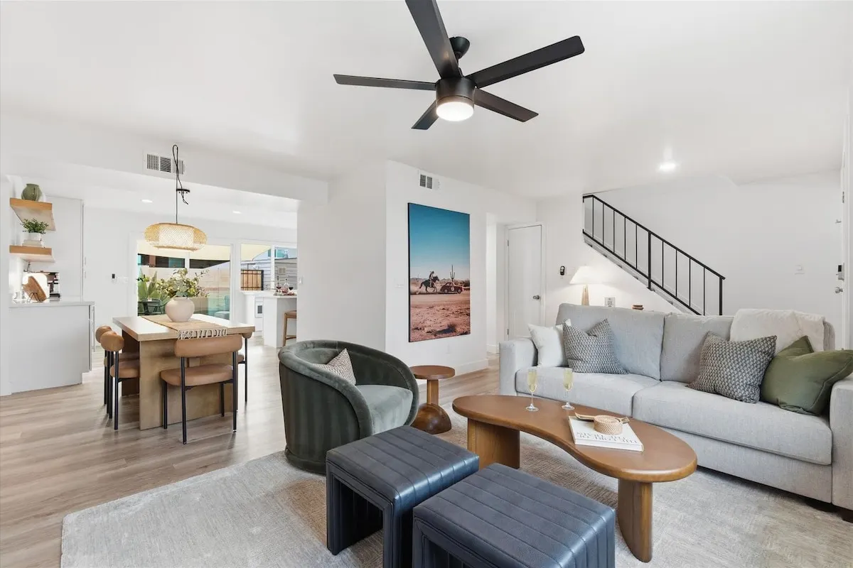 Bright open living room at Hideaway with a deep sofa, a green velvet chair, leather ottomans and the dining table beyond