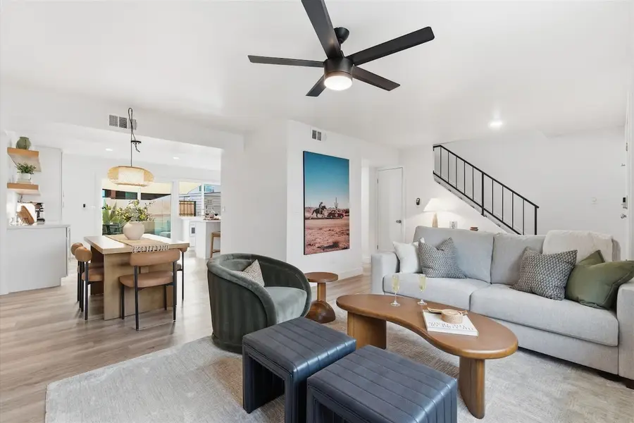 Bright open living room at Hideaway with a deep sofa, a green velvet chair, leather ottomans and the dining table beyond