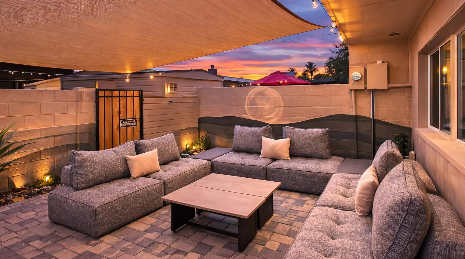 Private back patio at Hideaway at sunset, with a sectional under a shade sail, string lights and a desert mural painted on the block wall