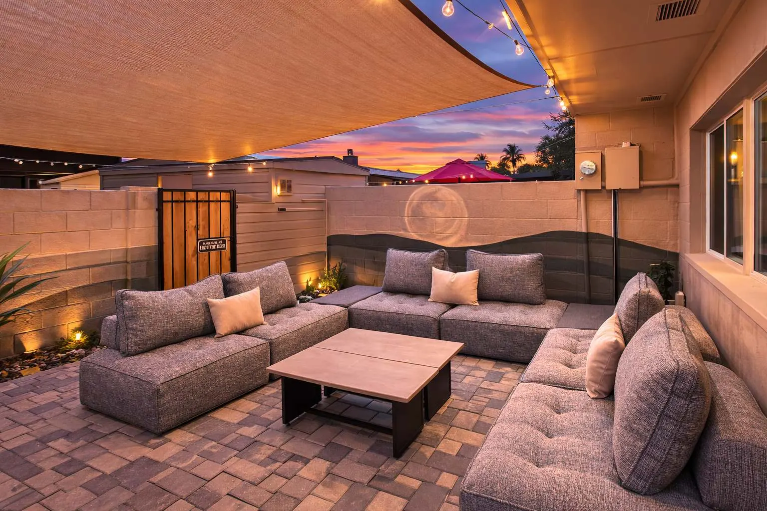 Private back patio at Hideaway at sunset, with a sectional under a shade sail, string lights and a desert mural painted on the block wall