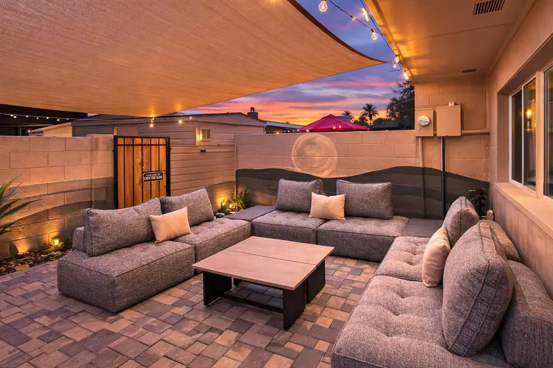 Private back patio at Hideaway at sunset, with a sectional under a shade sail, string lights and a desert mural painted on the block wall