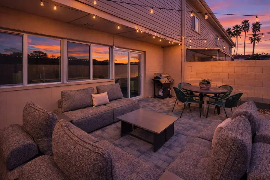 Whole private patio at Hideaway at sunset: sectional, coffee table, dining table and gas grill under string lights