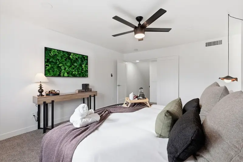 Primary bedroom at Hideaway from the doorway: king bed, wall-mounted smart TV, console table and ceiling fan